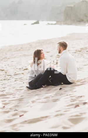 Happy man and woman sitting on sand near sea, romantic mood Stock Photo