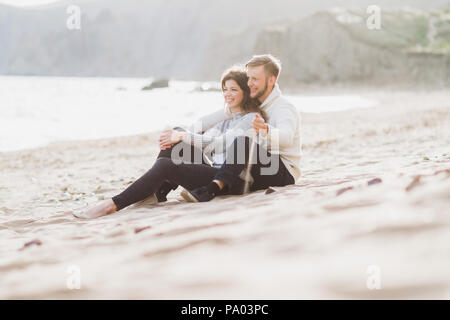 Happy man and woman sitting on sand near sea, romantic mood Stock Photo