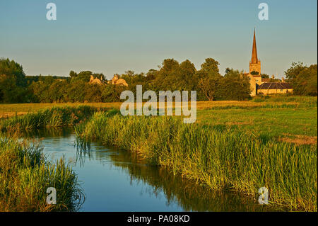 The River Windrush winding through water meadows towards the Cotswold town of Burford, with the church spire of St John the Baptist in the distance. Stock Photo