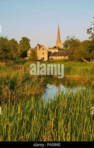 The River Windrush winding through water meadows towards the Cotswold town of Burford, with the church spire of St John the Baptist in the distance. Stock Photo