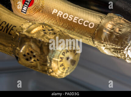 Close up on featured Prosecco name on foil neck sparkling wine bottle with Champagne bottle neck de-focused in foreground in chilled wine cabinet Stock Photo