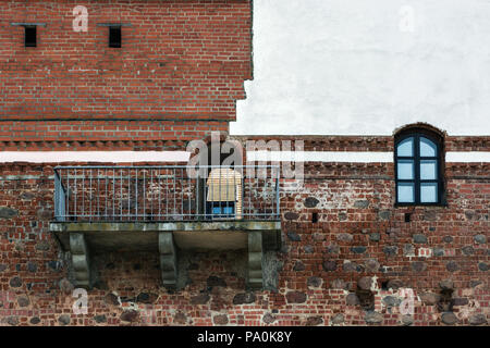 The old fortress wall of the Mir castle of red brick with a balcony and a window, partially covered with white plaster. Stock Photo