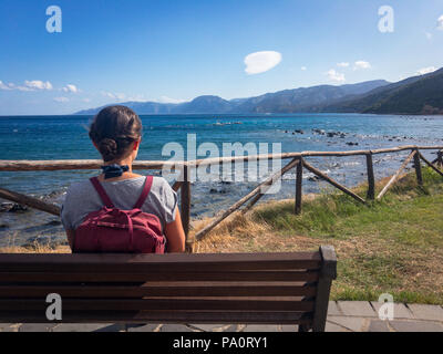 Woman with backpack on a bench looking at Gulf of Orosei south of Cala Gonone on the Italian island of Sardinia Stock Photo