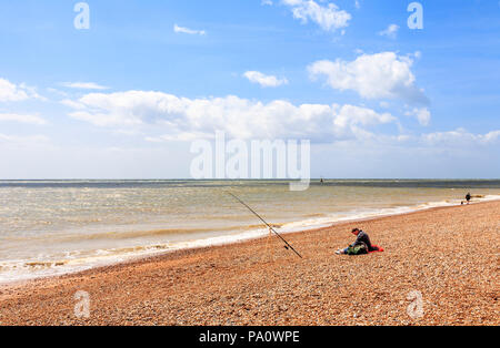 Lone sea fisherman fishing from the seashore on the shingle beach at Dungeness, Shepway district, Kent Stock Photo