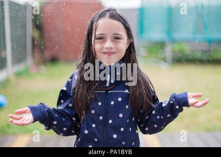 Celbridge, County Kildare, Ireland. 20th July 2018: After prolonged spells of hot weather with above average temperatures we might be getting first whole day of actual showers as sun stays hidden behind the clouds. Young girl enjoying the weather playing in rain in the garden. Stock Photo