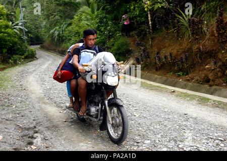 CAINTA, RIZAL, PHILIPPINES - OCTOBER 2, 2015: A young man and his companion ride a motorcycle along an uphill road. Stock Photo
