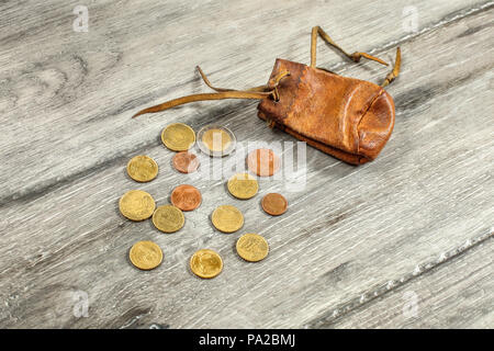 Old worn brown leather coin pouch,  with euro coins spilled on gray wood desk. Stock Photo