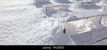 Winter snow loadings banner. Sun shining on desks and benches completely covered under deep snowfall. Stock Photo