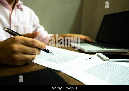 Businessman working at office with laptop and documents on the table, Businessman holding pens and papers taking notes in documents on the table. Stock Photo