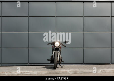 Craft motorcycle parking near gray wall of industrial building. Everything is ready for having fun driving the empty road on a motorcycle tour journey Stock Photo