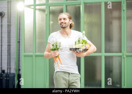 Man carrying box full of fresh raw vegetables just bought at the local market outdoors on the green background Stock Photo