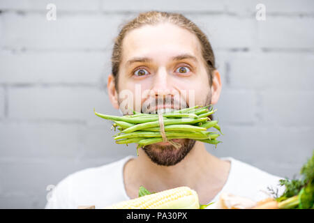 Close portrait of a handsome man biting green beans on the brick wall background Stock Photo