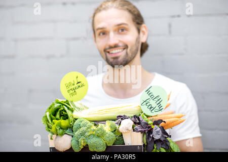 Portrait of a handsome man holding box full of fresh vegetables on the brick wall background Stock Photo