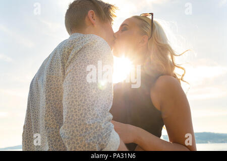 Romantic couple kissing on beach against the sun Stock Photo