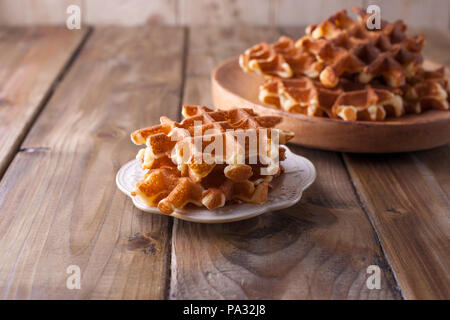 Sweet Belgian waffles for breakfast, on a wooden plate. On a brown wooden background. Stock Photo