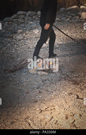 cropped view of adult male tending to an outdoor fire on a pebble beach by the Herault river, France Stock Photo
