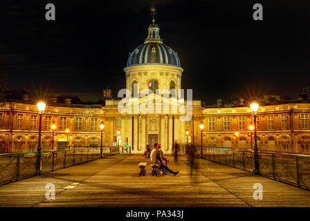 Pont des Arts bridge to Institut de France building, a French learned society group of five academies. Crossing bridge point of view with people in Paris, France. Night scene. Stock Photo
