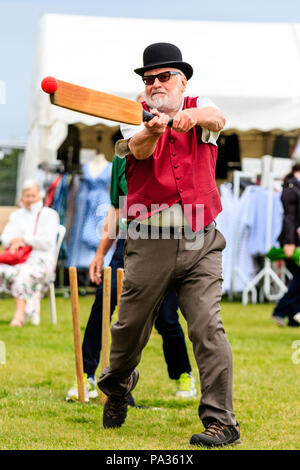 Senior man dressed in Victorian clothing as a Charles Dickens character, batting with a cricket bat during a match. Wears modern trainers and sunglass Stock Photo