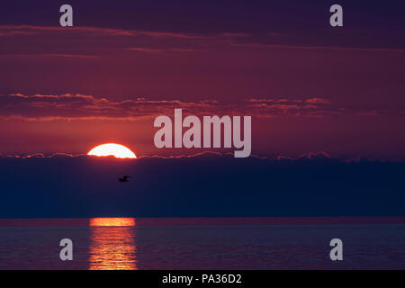 Sunset and setting sun over sea from Penmon Point on Anglesey with beautiful reflection on the sea surface, Anglesey, Wales Stock Photo
