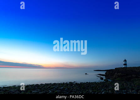 Last light and sunset at Penmon Point with the James Walker designed Trwyn Du Lighthouse on the shoreline as the sun sets across the Irish Sea Stock Photo