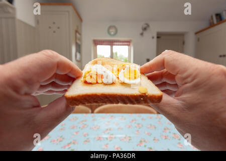 A point of view person holding a piece of bread with fresh made hard boiled egg with white and yoke on moving towards the persons mouth Stock Photo