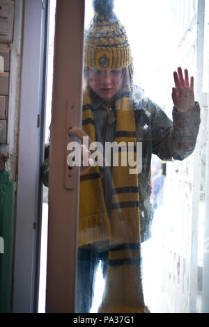 emotive low angle shot of ten year old boy dressed in winter clothes coming into his home after snowball fight Stock Photo
