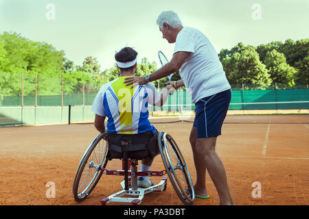 tennis coach teaching a disabled player the correct movement of the backhand outdoor Stock Photo