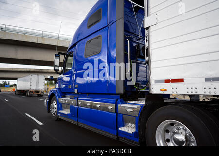 Big rig modern bright blue long haul semi truck with refrigerator semi trailer transporting perishable and frozen foods on the wide highway road with  Stock Photo