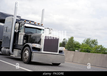 Black classic American bonnet powerful stylish big rig semi truck with vertical exhaust pipes and chrome accent parts on cab with sleeping place for t Stock Photo