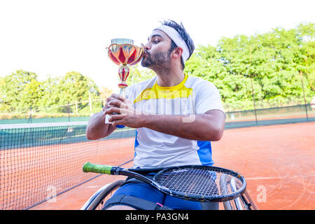 young disabled tennis player kisses the cup after winning the outdoor tournament Stock Photo