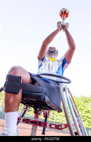 young disabled tennis player raises the cup to the sky after winning the outdoor tournament Stock Photo