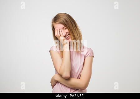 Studio shot of good looking young female giggles joyfully, covers mouth as tries stop laughing. Stock Photo