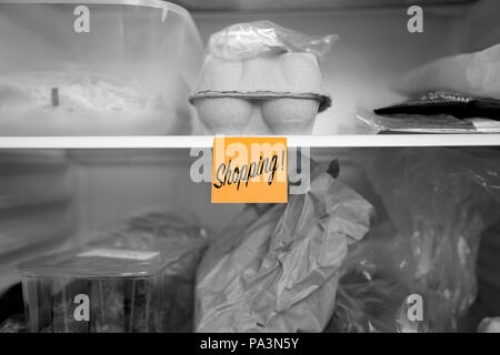 Shopping written on a sticky note  stuck on a fridge shelf with food.  Abstract with selective colour Stock Photo