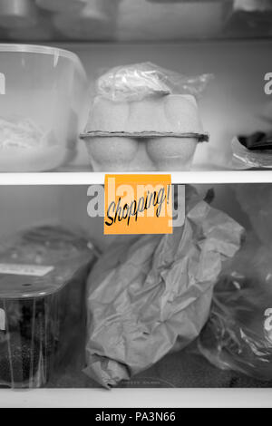 Shopping written on a sticky note  stuck on a fridge shelf with food.  Abstract with selective colour Stock Photo