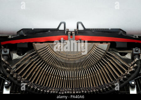 close vintage typewriter black and red ribbon and typebars ready to type on a blank textured sheet