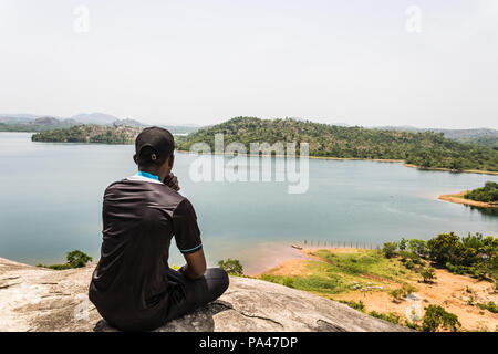 A sport man sitting on top of a mountain and looking ahead at the river and island Stock Photo
