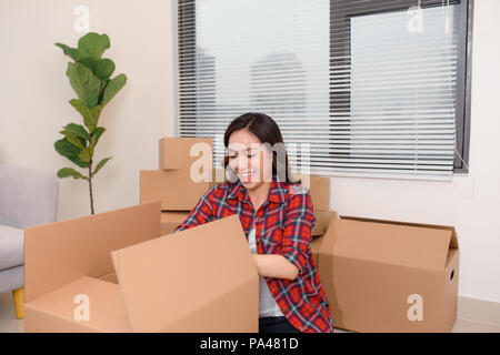 Excited young asian woman unpacking carton boxes with cozy home stuff in new apartment. Stock Photo