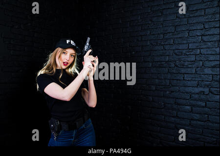 FBI female agent in cap and with gun at studio against dark brick wall. Stock Photo