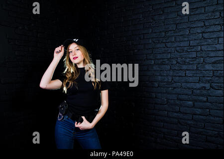 FBI female agent in cap and with gun at studio against dark brick wall. Stock Photo