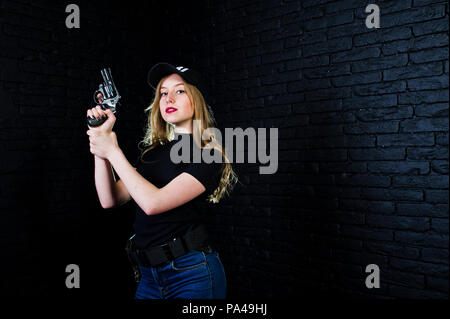 FBI female agent in cap and with gun at studio against dark brick wall. Stock Photo