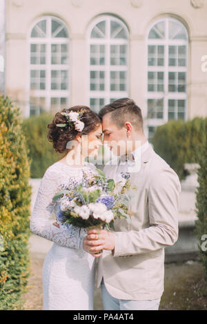 Happy young newlyweds embracing near the old beige house with columns and big vintage windows. Romantic wedding in Paris Stock Photo