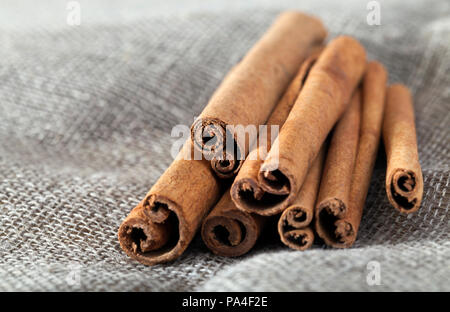 folded together a few brown and very fragrant cinnamon sticks lying on flax material, a close-up of spices and seasonings used in cooking Stock Photo