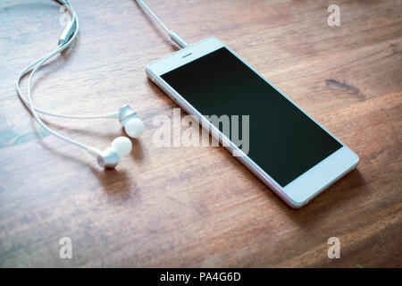 White Smartphone With Plugged In Headset On Wooden Table Stock Photo