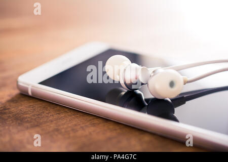 In-Ear Headphones Lying On Top Of A White Smartphone On A Wooden Table Stock Photo