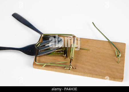 Cutlery and mousetrap on a white table. Fork and spoon caught in a trap. White background. Stock Photo