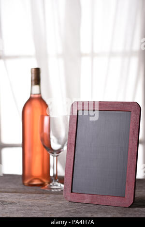 A bottle of blush wine with a blank menu board, on a rustic wood table in front of a window. Perfect for a Wine Menu or Wine Tasting announcement. Stock Photo