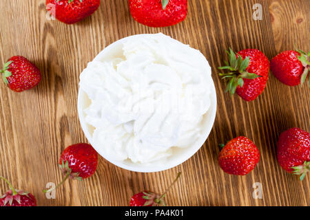 wooden table with strawberries and cream in a white bowl, close-up on top Stock Photo