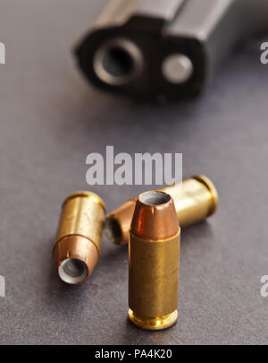 Three 40 caliber hollow point bullets on a black background with a black pistol laying behind them showing only it's muzzle Stock Photo
