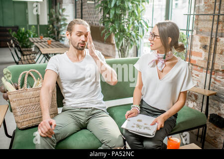 Man having headache sitting during the conversation with young woman on the sofa indoors Stock Photo