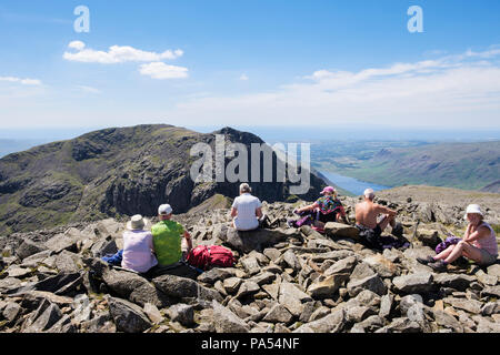 Hikers group resting on Scafell Pike summit looking towards Scafell's Broad Stand & Scafell Crag in Lake District National Park Cumbria England UK Stock Photo